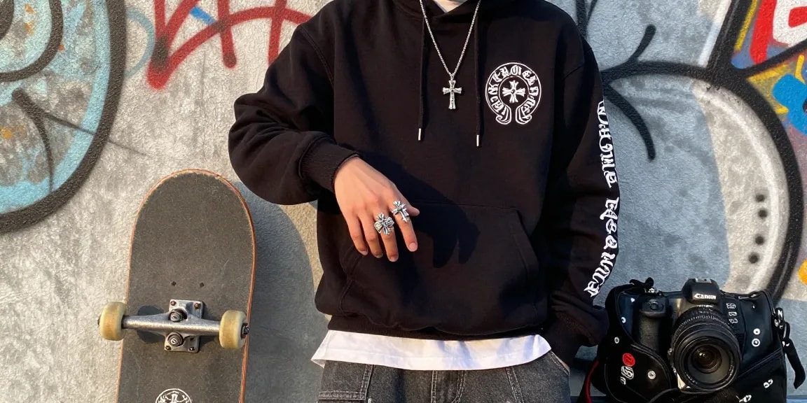 Stylish individual showcasing Chrome Hearts hoodie and accessories against urban graffiti backdrop.